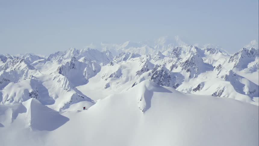 Aerial pull away from person walking on a mountain ridge over a huge winter vista