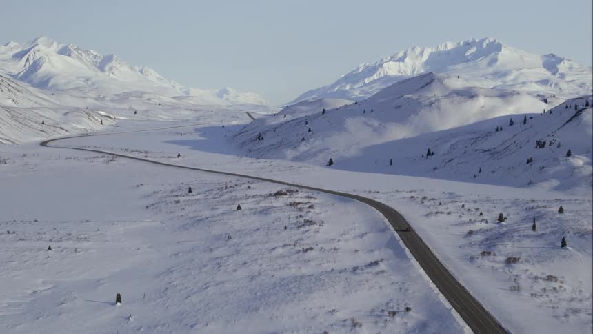 Aerial of a car on a highway cutting through huge mountains in winter