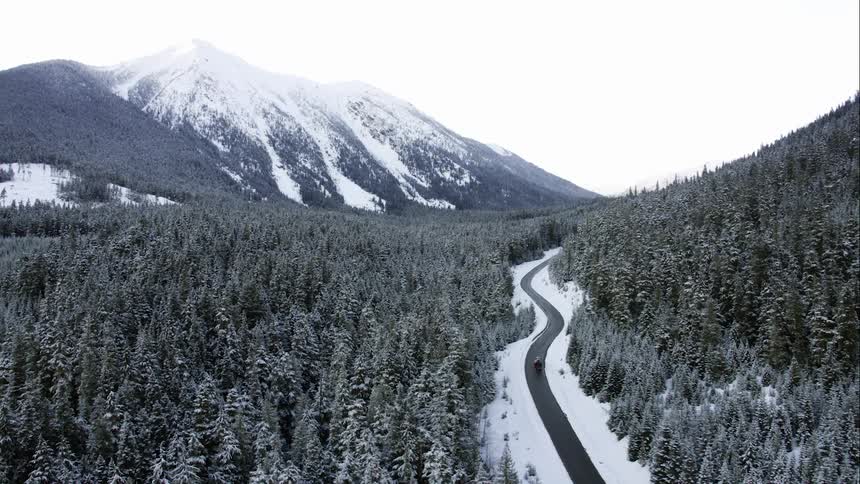 A vehicle driving on a winter road in a massive mountain landscape