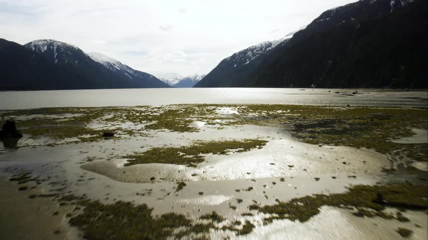 Aerial push over tidal area and ocean in front of snow capped mountain range