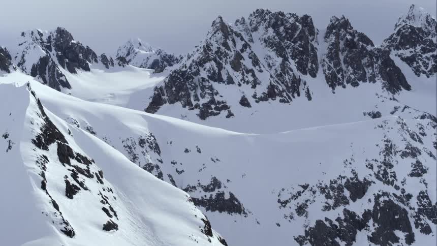 Aerial of a mountain ridge covered in snow under a pale sky