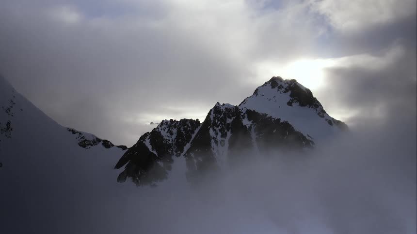 Aerial of fog around a snowy mountain at sunset
