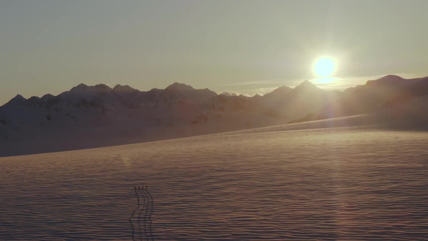 Four skiers in a vast glacial field at sunset