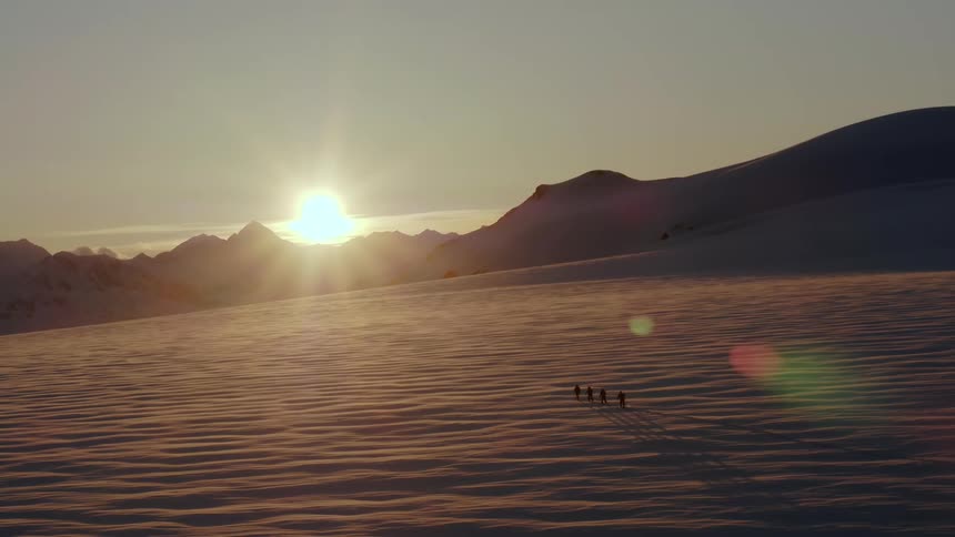 Four people skiing through an endless glacial field at sunset