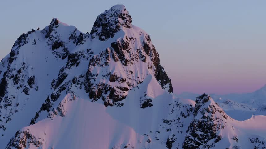 Aerial of snowy mountain peaks in pink sunset light