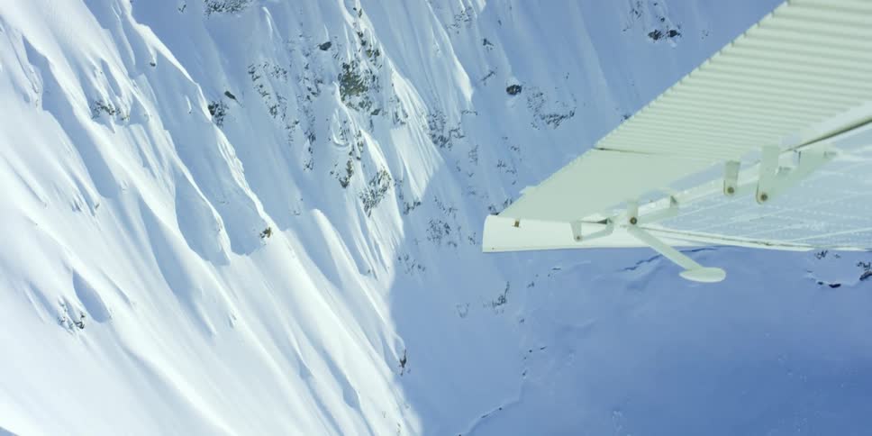 Wing of a plane flying over the snow covered slopes of a mountain range