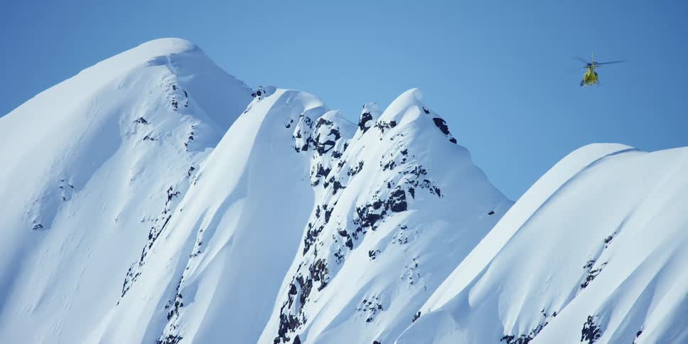 A helicopter is flying above a snow covered mountain