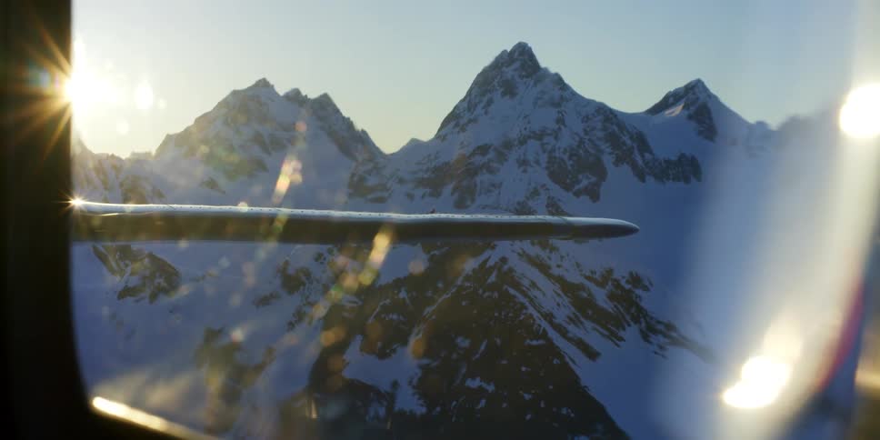 A plane flying over a snowy mountain range on a sunny day