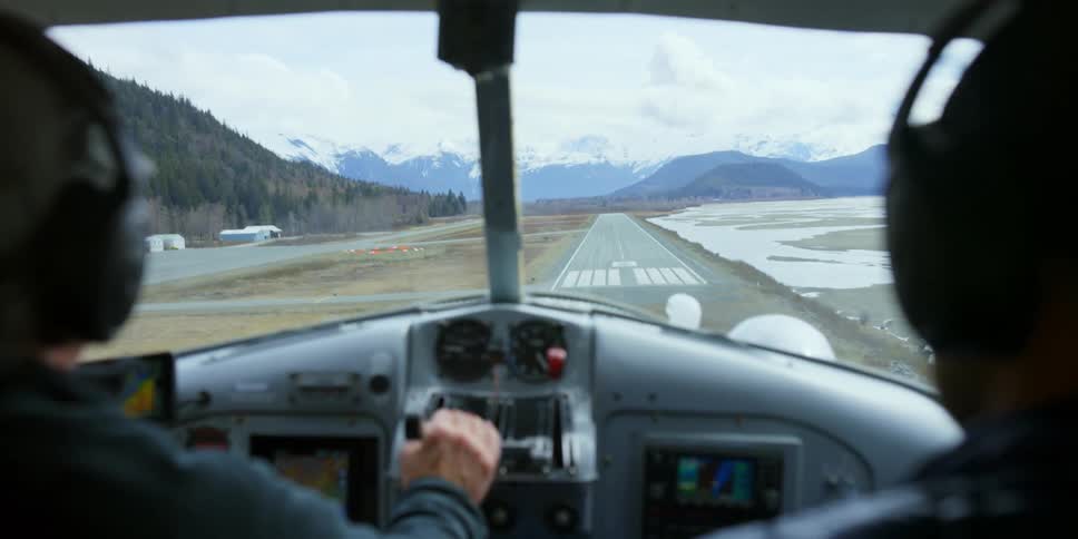 A pilot lands a small plane on an airstrip near mountains