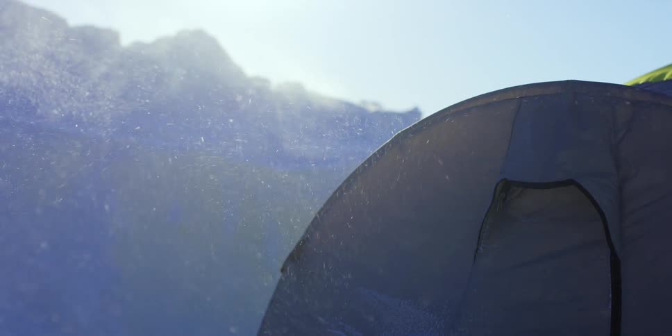 Snow falling on a tent at the base of a mountain