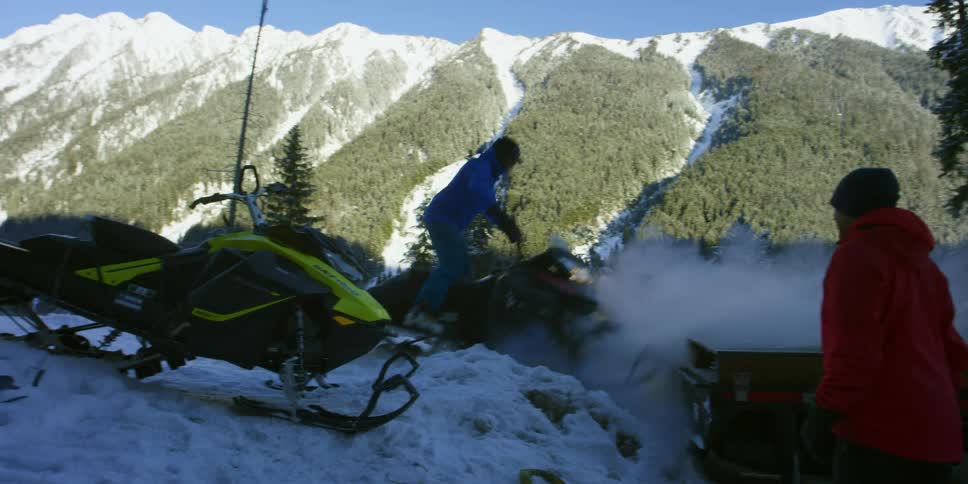 A man riding a snowmobile near other men and snowmobiles