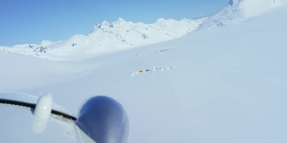 An airplane flying over snow covered tundra with a mountain range in the background