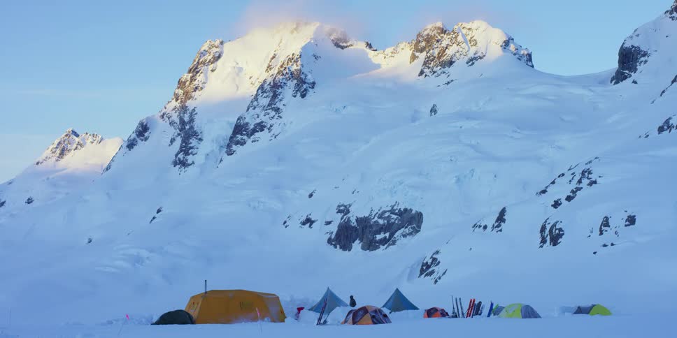 A person walking around a campsite set up a the base of a snowy mountain