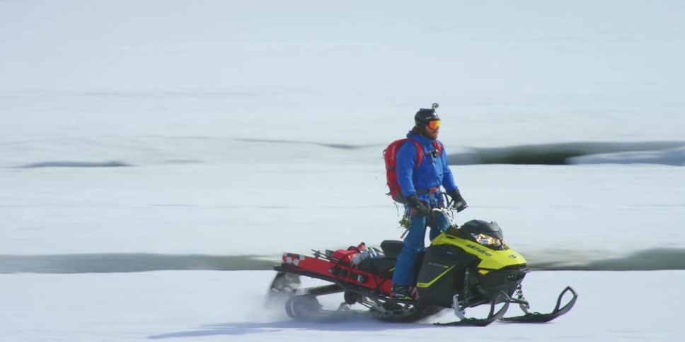 Two people ride snowmobiles on a snow and ice terrain