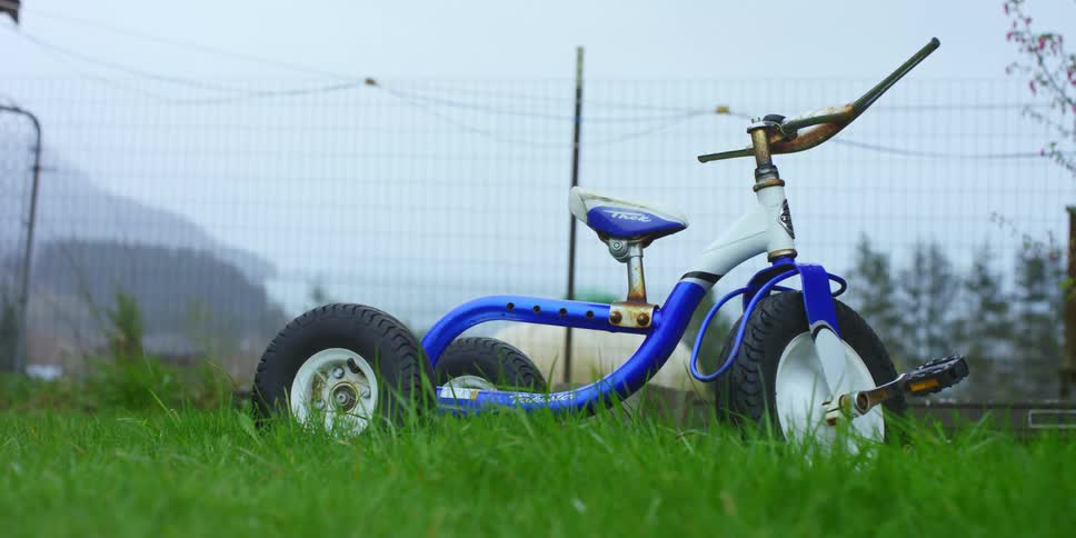 A childrens tricycle in a yard surrounded by wire fencing on a foggy day