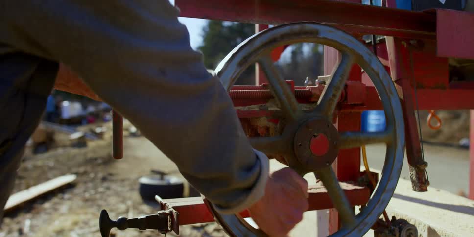 A white man works with a hand powered machine outside near a dirt road