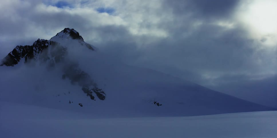 Clouds travel over a mountain peak covered in snow