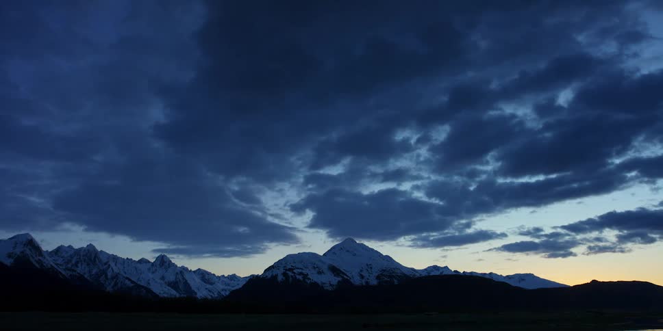 A time lapse of clouds moving over a snow covered mountain range