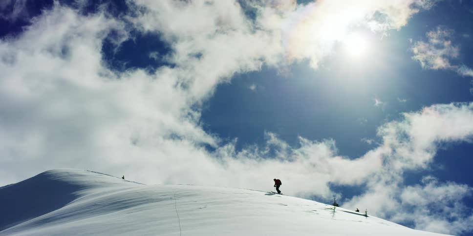 Person hikes towards mountain summit on skis