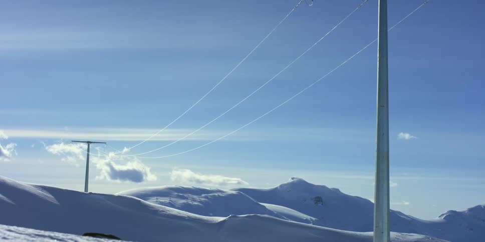 Power lines and poles in front of snow covered mountains