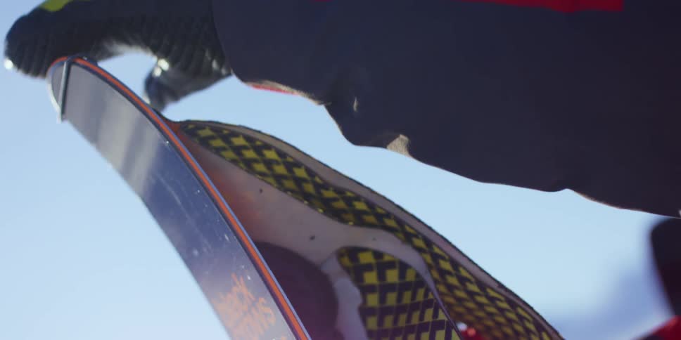 Skier applies backing to ski without removing gloves against white backdrop