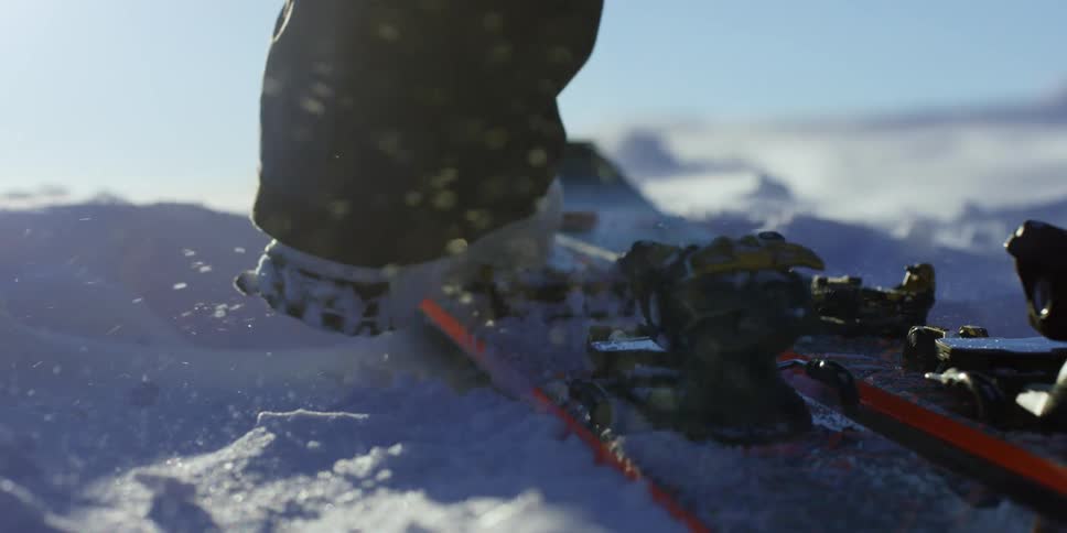 A person kicks snow off their boot as they slip their foot in to their ski