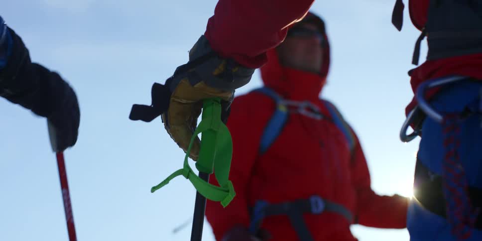 Three people are traveling with ski sticks on a sunny day