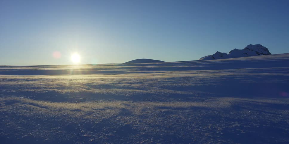 The low sun shines on a vast field of snow under a clear sky