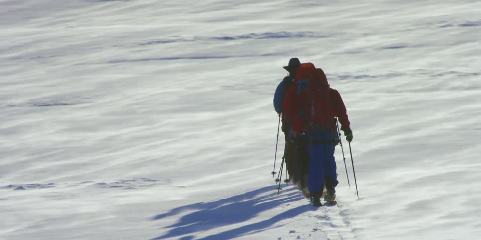 Group of men walk on skis in a single line over the frozen plains covered in snow