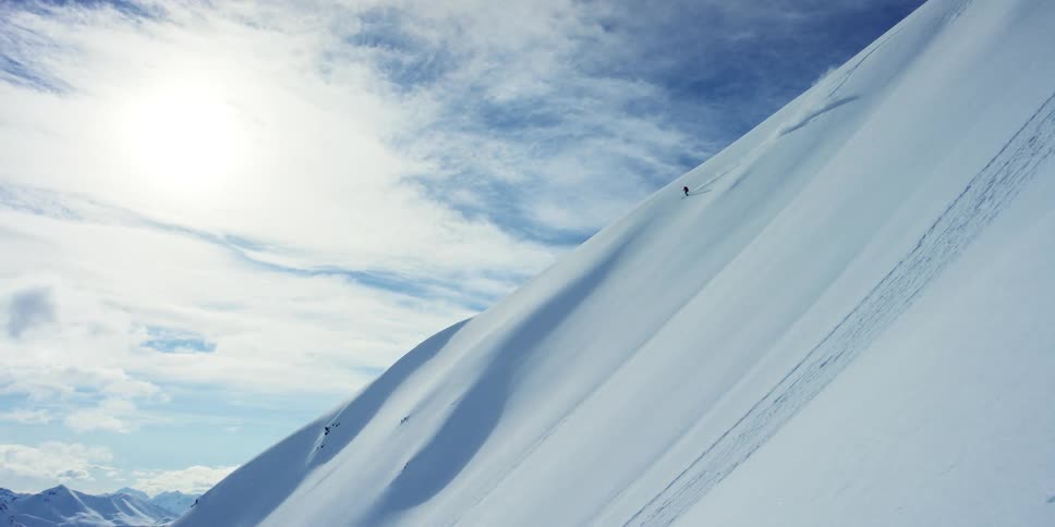 A snowboarder descends a smooth mountain slope on a sunny day