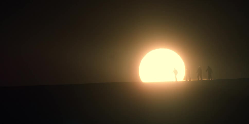 Setting sun silhouettes a group of skiers walking on frozen plains