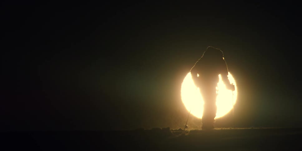 Person cross country skiing silhouetted against sun