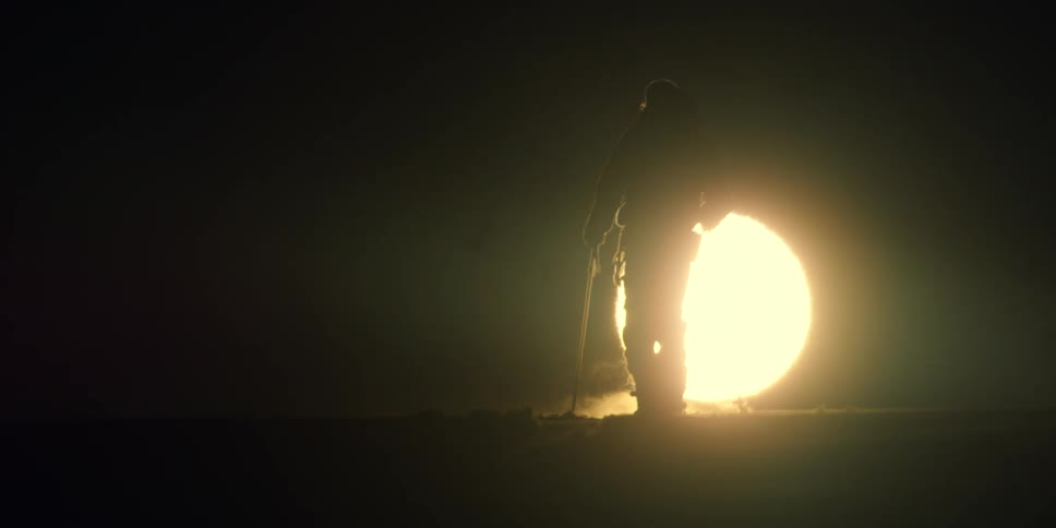 A skier stands in front of a large spotlight on a mountain at night