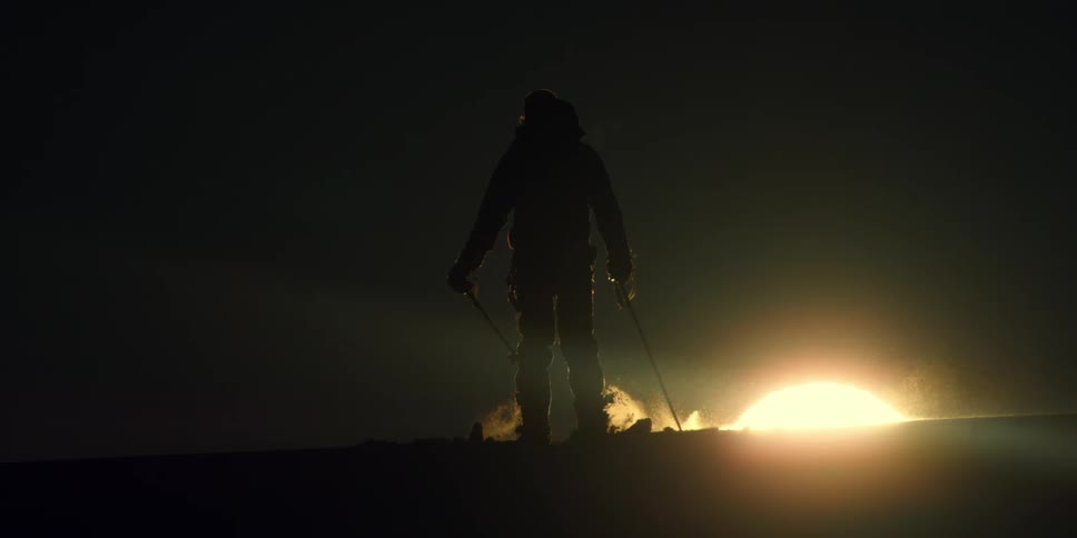 A silhouette of a person walking on skis with the sky and the sun in the background