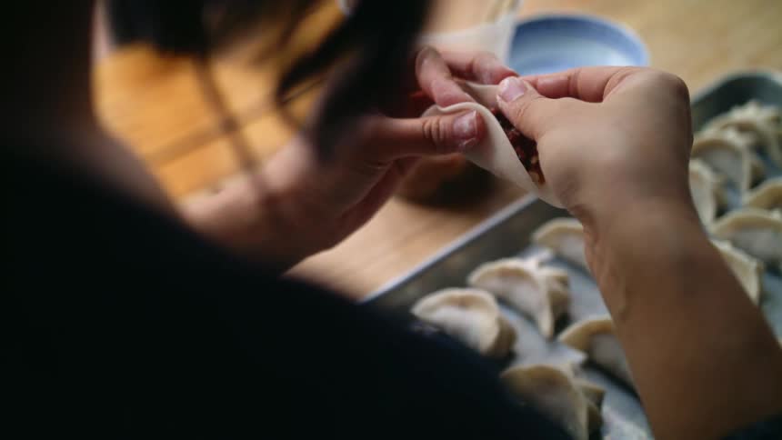 A woman wraps up a dumpling filled with meat and vegetables to add to a baking sheet full of dumplings