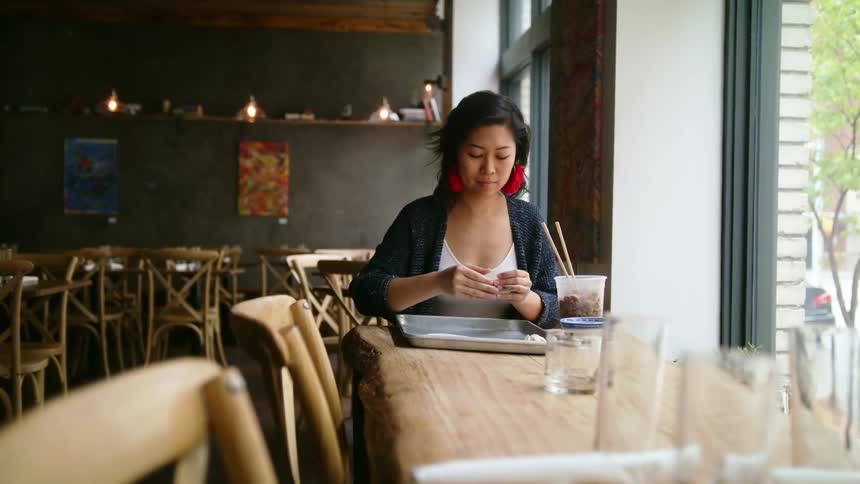 Young woman prepares food at table inside empty restaurant