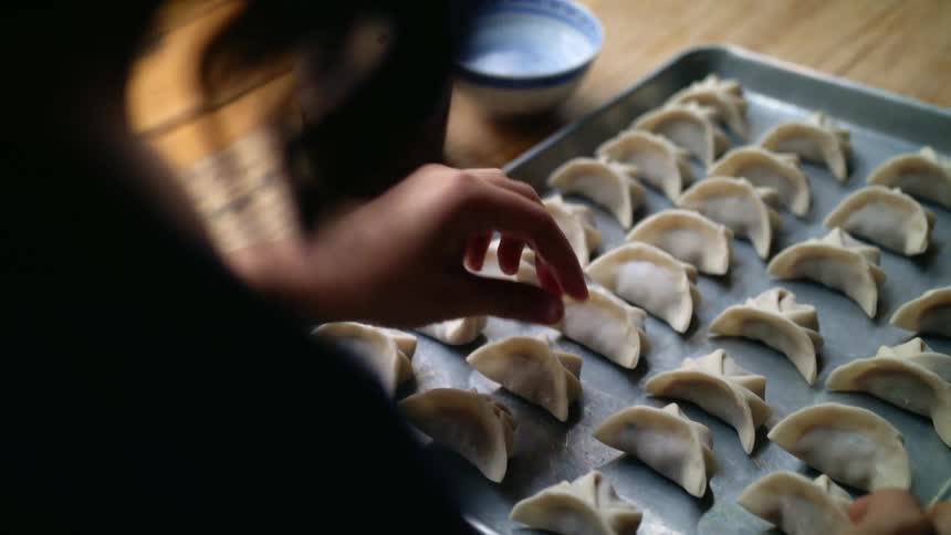 A woman folds chinese dumplings and places them on a pan in preparation for cooking them