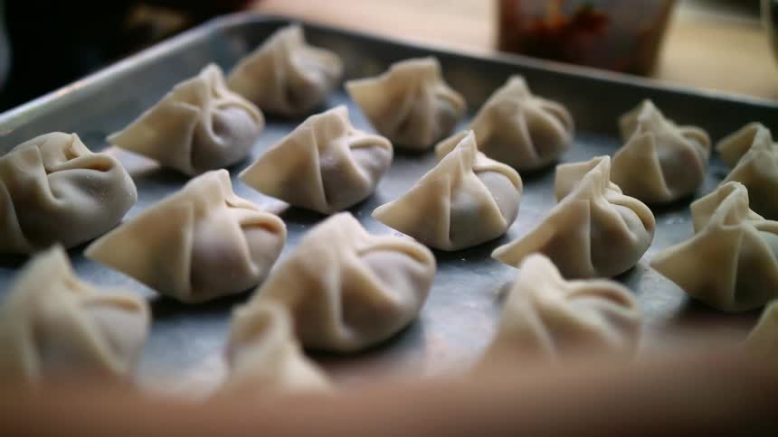Rows of folded dumplings sit on metal sheet with slightly raised rim