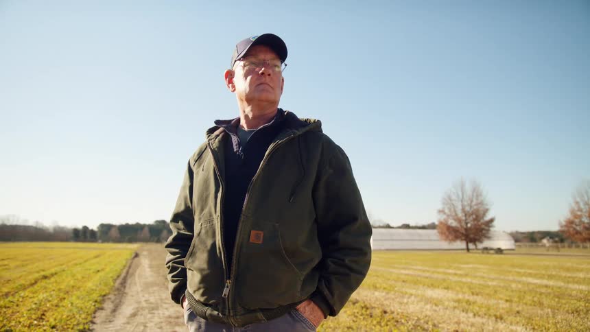 A farmer stands and poses in a dirt trail running through his crops