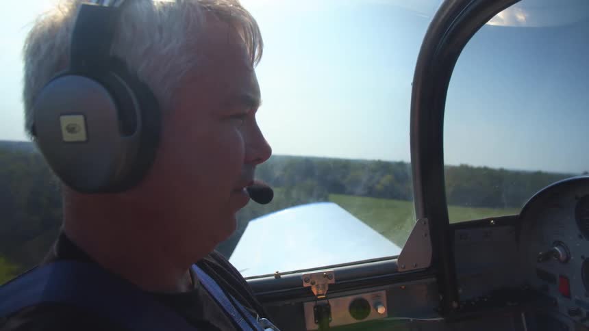 Man wearing headset pilots plane over fields and forest stretching to the horizon