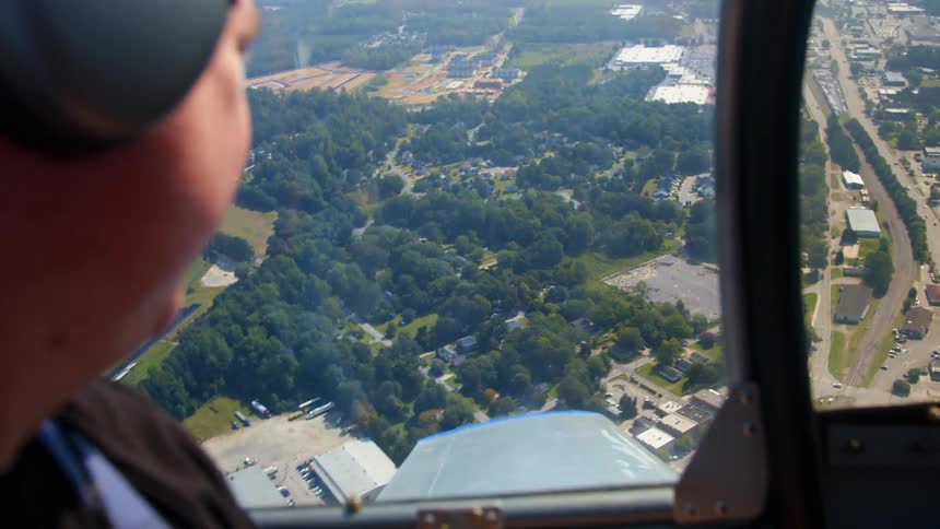A person with a headset flying on a plane with trees and streets in the background