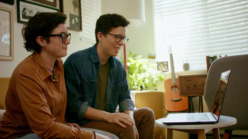 Man and woman smile and wave as they video chat on a laptop