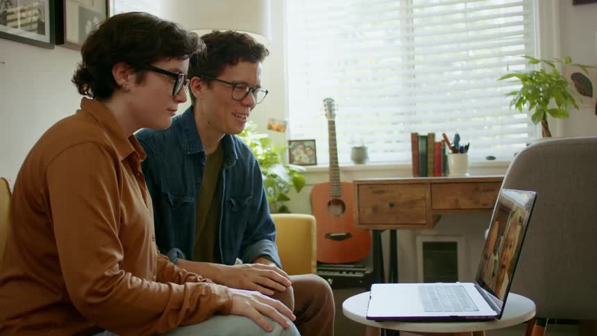 Young couple video chats with older couple on laptop in living room