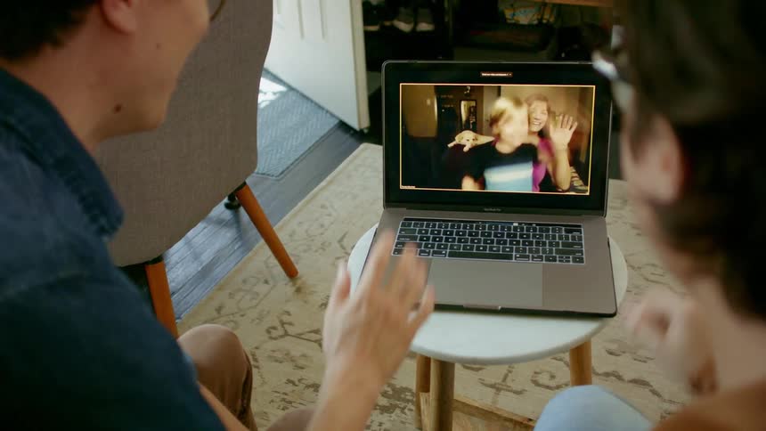 A man and woman sit together in a living room as they use a laptop to video chat with a woman and her young son