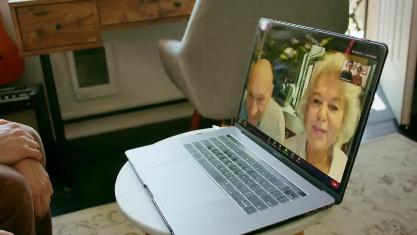 A person sits in front of a laptop having a video call with an elderly couple