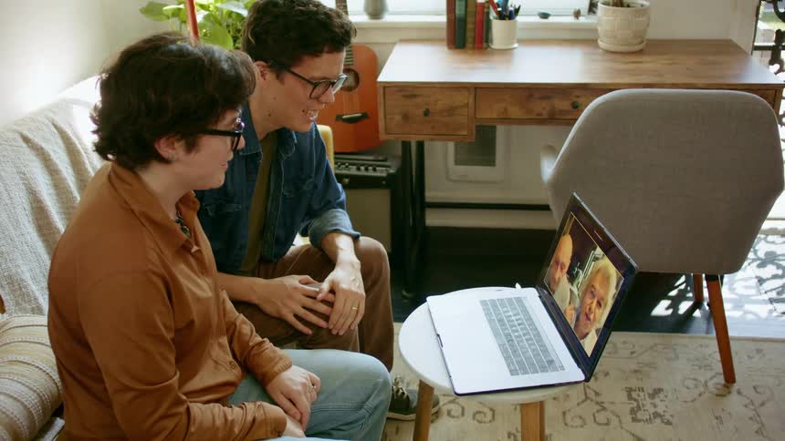 Young couple sitting in a couch in the living room talks to their parents on a video call
