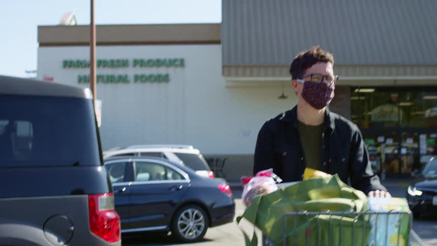 A person pushes their cart of bagged groceries to their vehicle in a grocery store parking lot