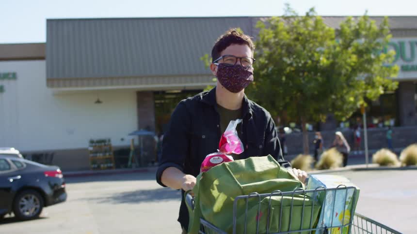 A man wears a face mask as he pushes a cart full of groceries through a parking lot outside the market