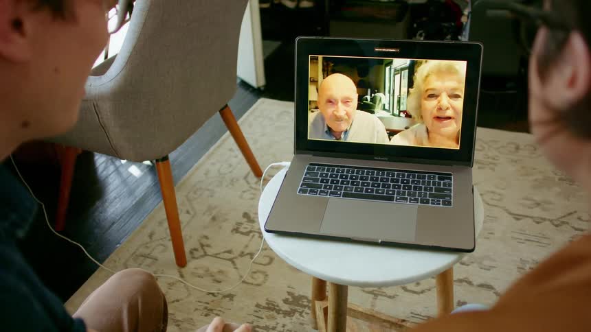 A couple of young adults communicate with an elderly couple via video chat on their laptop