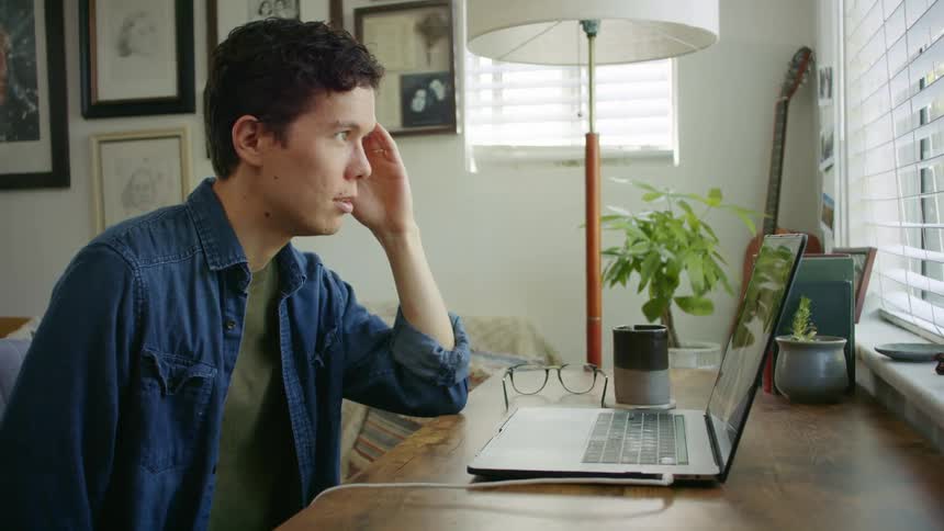 A man sitting at a desk in his home carries on a conversation via his laptop
